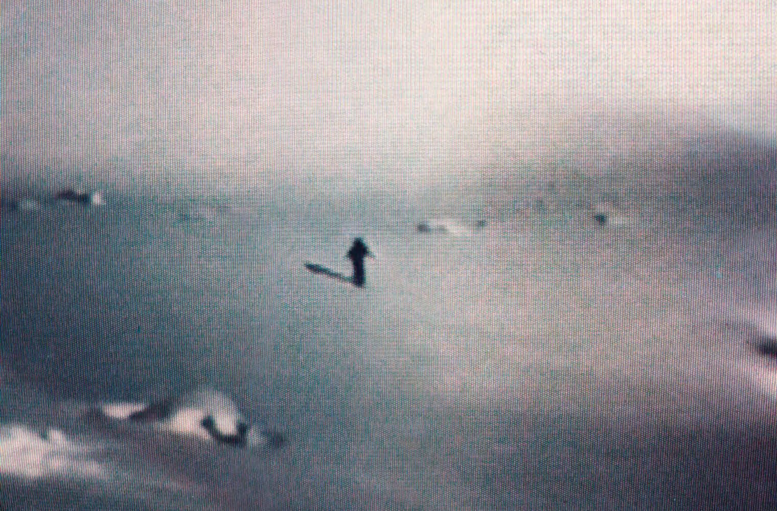 Ein Bild, das im Videostill gehalten ist. Eine Person steht in der Ferne auf einer Schneefläche. Der Schatten der Person ist gut erkennbar. 