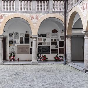 Arkadengang im Innenhof von Schloss Hartheim. An der Wand hängen Gedenksteine. Am Boden stehen Blumengestecke.