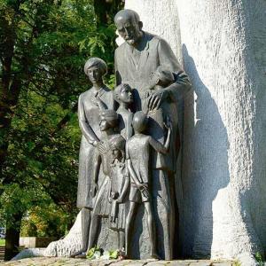 Das Denkmal zeigt Janusz Korczak. Er steht vor einem großen Baum und hält seine Hände schützend um sechs Kinder unterschiedlichen Alters.