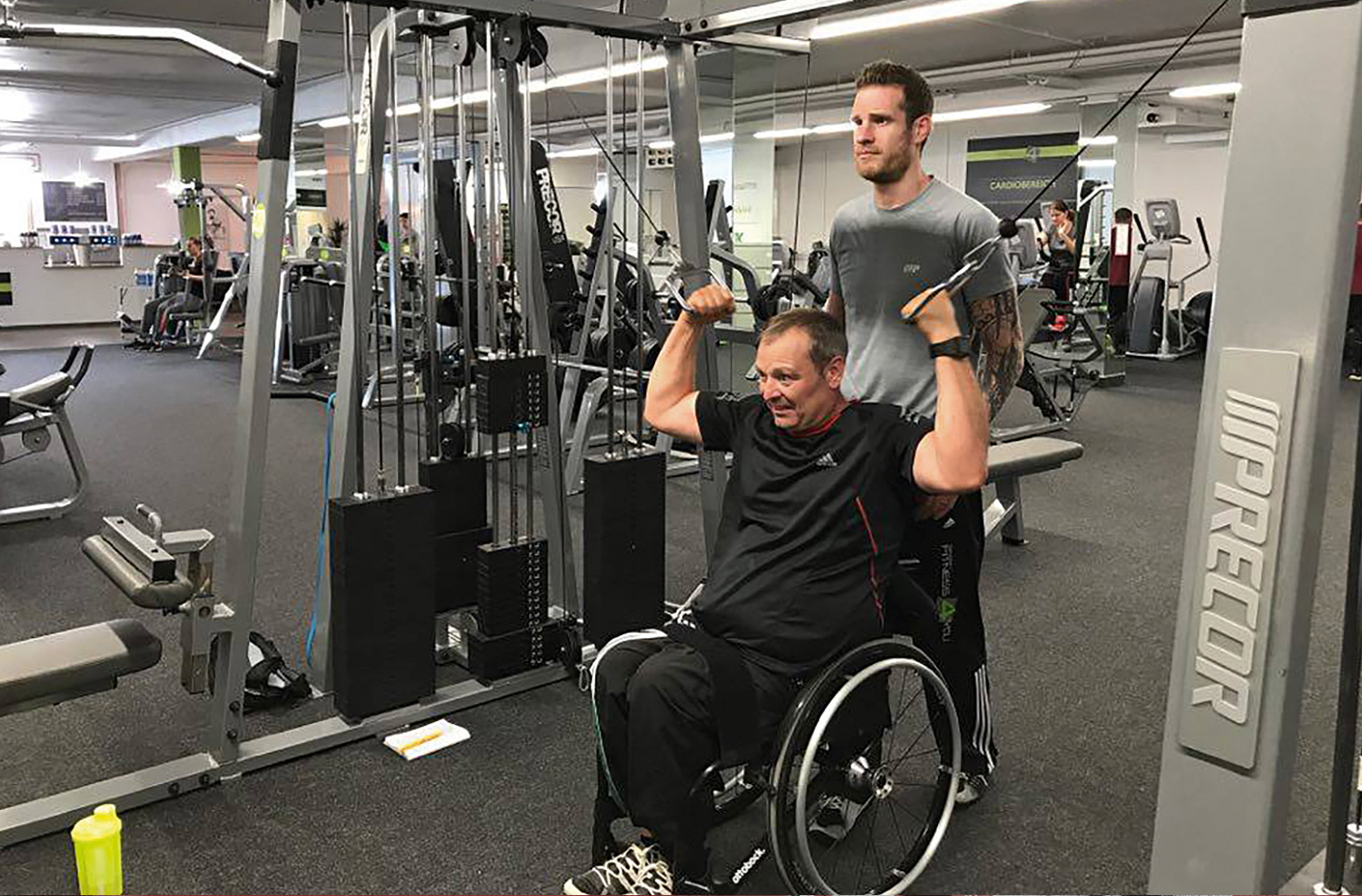 Der ehemalige Rollstuhlbasketballer Dirk Schmitz übt an einem Fitnessgerät. Sein Trainer Thomas Gessler steht dahinter.