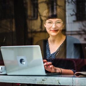 Die Journalistin und Bloggerin Mareice Kaiser sitzt hinter einem großen Fenster und arbeitet am Computer. - Foto: Carolin Weinkopf