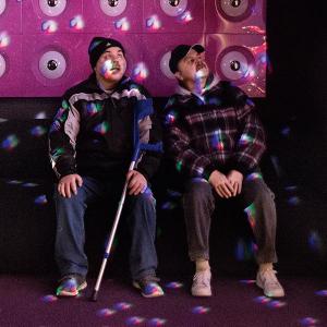 Die taubblinden Zwillingsbrüder Jörg und Rolf Fischer sitzen in einem in farbiges Licht getauchten Raum und spüren die Lichtreflexe. 