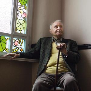 Ein älterer Herr sitzt auf einem Sessel im Eck eines Stiegenaufganges.