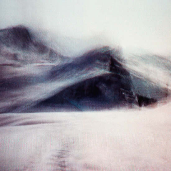Ein Bild im Videostil zeigt eine Sand- oder Schneedüne, die über einen Gipfel fegt. Der Himmel ist weiß.