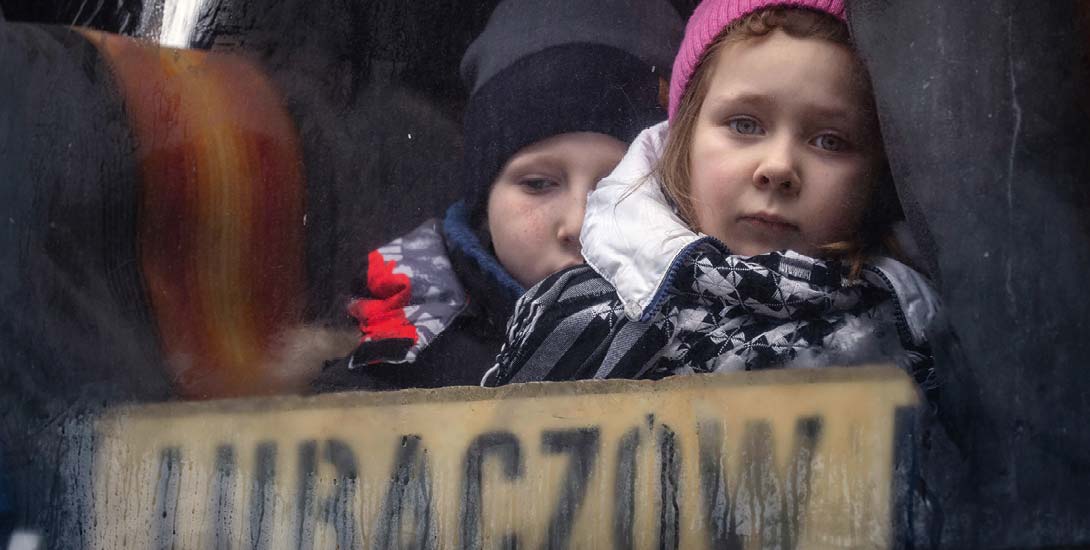 Ein Bub und ein Mädchen im Alter von 7 bis 10 Jahren schauen mit großen, traurigen Augen aus einem Zugfenster.