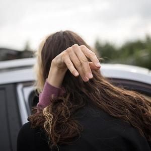 Eine Frau – sie hat MS – wird aus dem Auto gehoben. Ihre rechte grazile Hand hält sich an der Schulter einer anderen Frau fest.