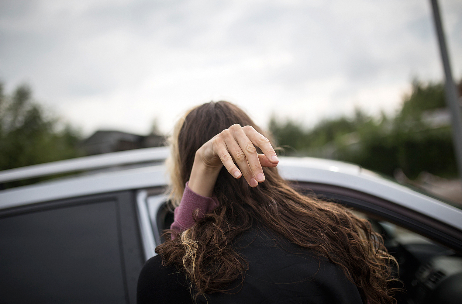 Eine Frau – sie hat MS – wird aus dem Auto gehoben. Ihre rechte grazile Hand hält sich an der Schulter einer anderen Frau fest.