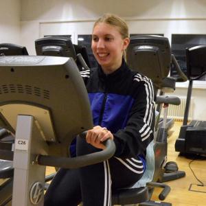 Eine junge Frau mit zufrieden lächelndem Gesicht auf einem Fahrradfitnessgerät und strampelt.