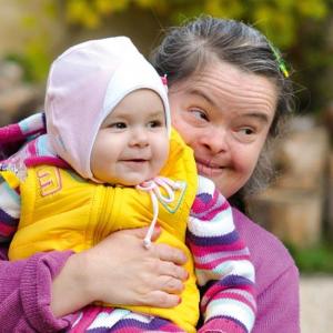 Eine Mutter mit Lernschwierigkeiten hält ihr einige Monate altes lächelndes Kind fröhlich im Arm.