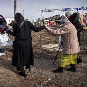 Das Bild zeigt zwei ältere Frauen, die über eine völlig vom Krieg zerstörte Straße gehen. 