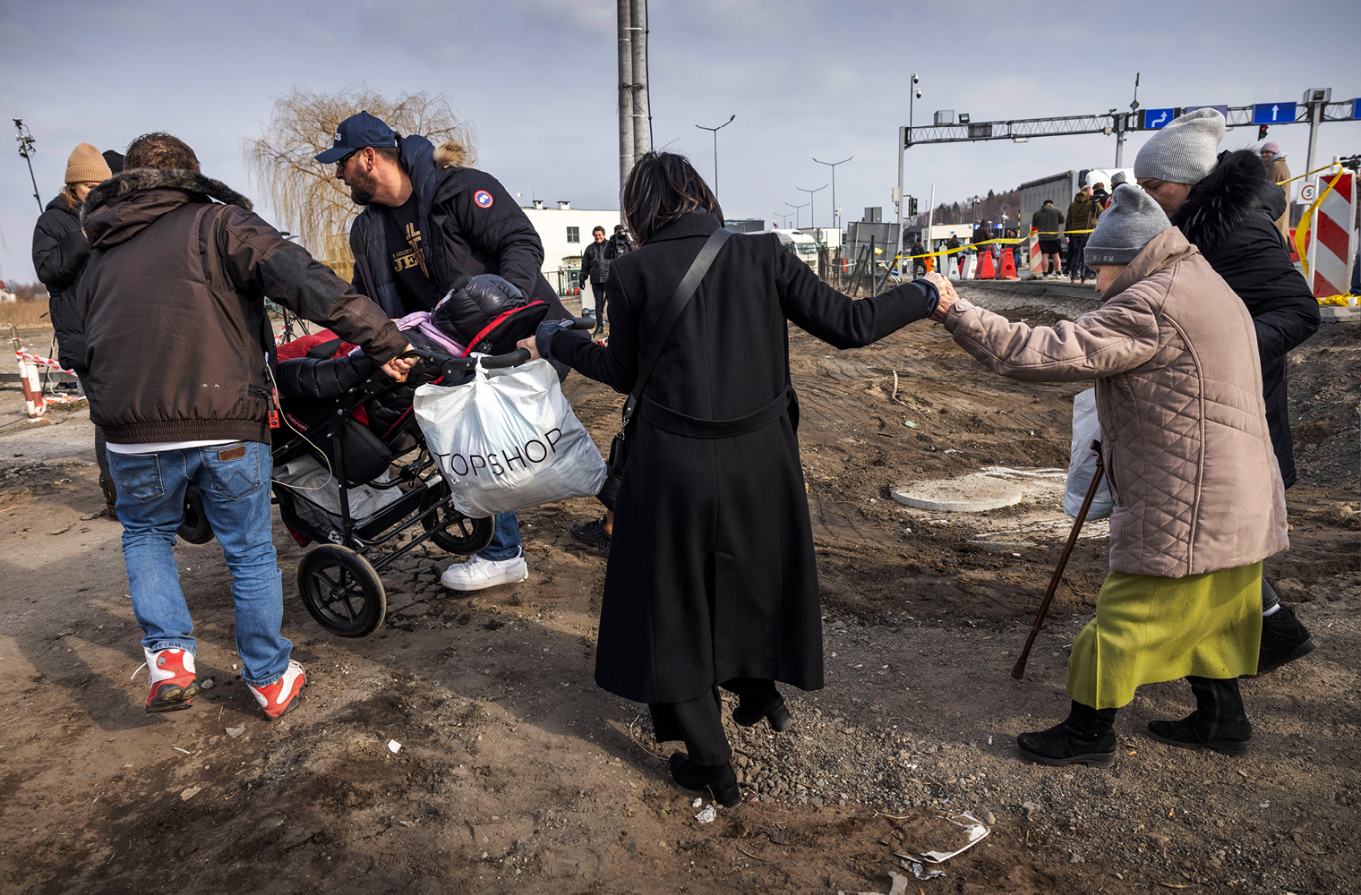 Das Bild zeigt zwei ältere Frauen, die über eine völlig vom Krieg zerstörte Straße gehen. Auch zwei Männer sind zu sehen, die einen Kinderwagen über das zerstörte Gelände hiefen. 
