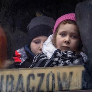 Ein Bub und ein Mädchen im Alter von 7 bis 10 Jahren schauen mit großen, traurigen Augen aus einem Zugfenster.