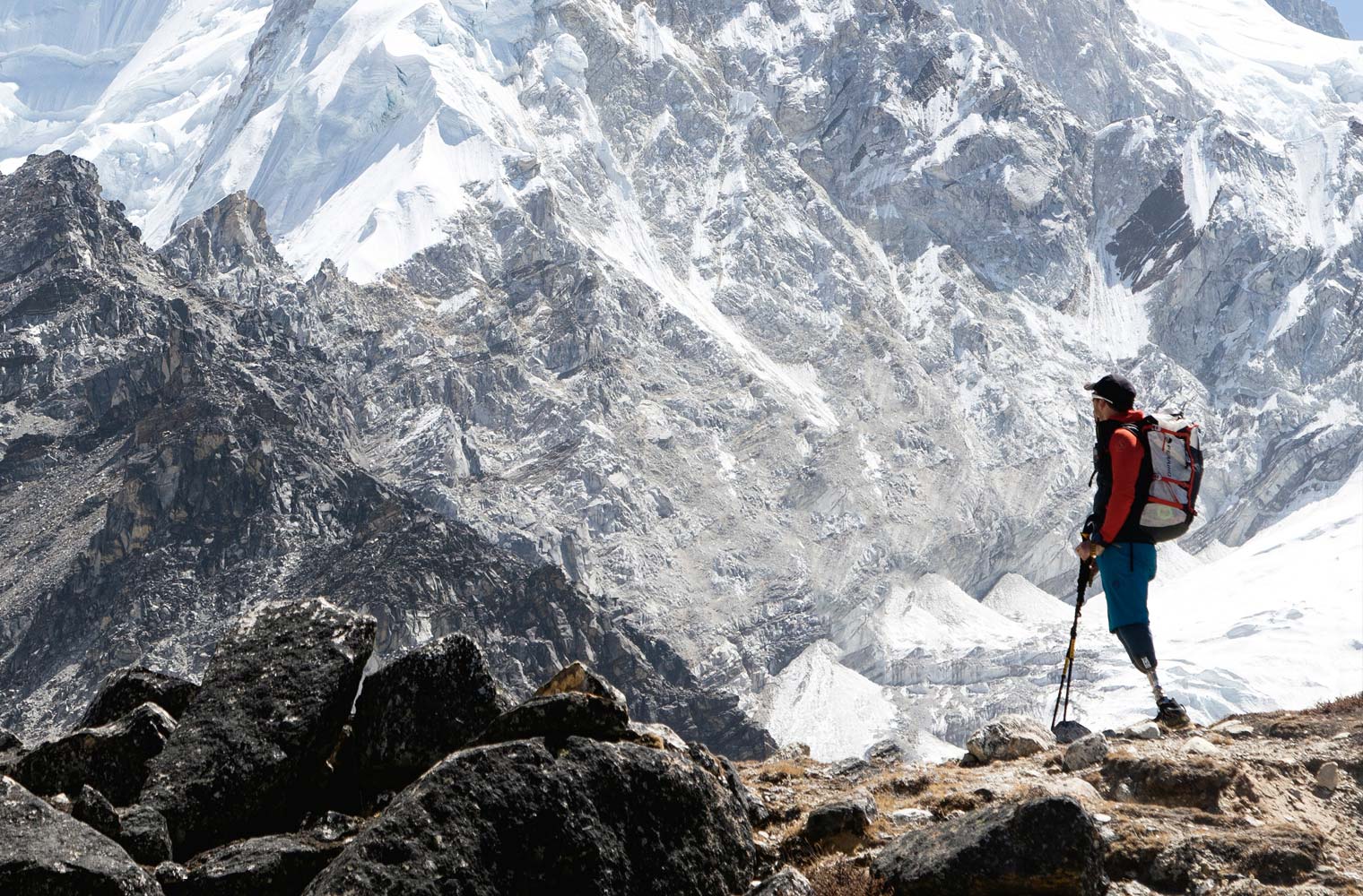 Ein Mann steht mit seinen zwei Beinprothesen an einem Bergrücken und sieht in Richtung eines schneebedeckten Gipfels. 
