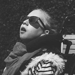 Lotta mit Sonnenbrille sitzt auf einer Parkbank und schaut staunend, mit leicht geöffnetem Mund in den Himmel.