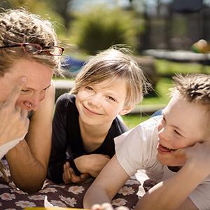 Willi,  seine Schwester Olivia und Mama Birte Müller liegen miteinander spaßend auf einer Decke im Gras.