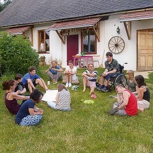 Zwölf Menschen – einer im Rollstuhl, einer mit Trisomie 21 – sitzen im Halbkreis in der Wiese und genießen ihr Zusammensein.